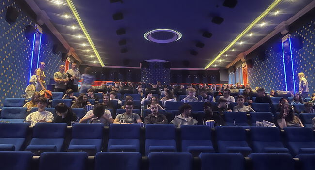 Schülerinnen und Schüler sitzen auf Kinostühlen (Raumansicht)