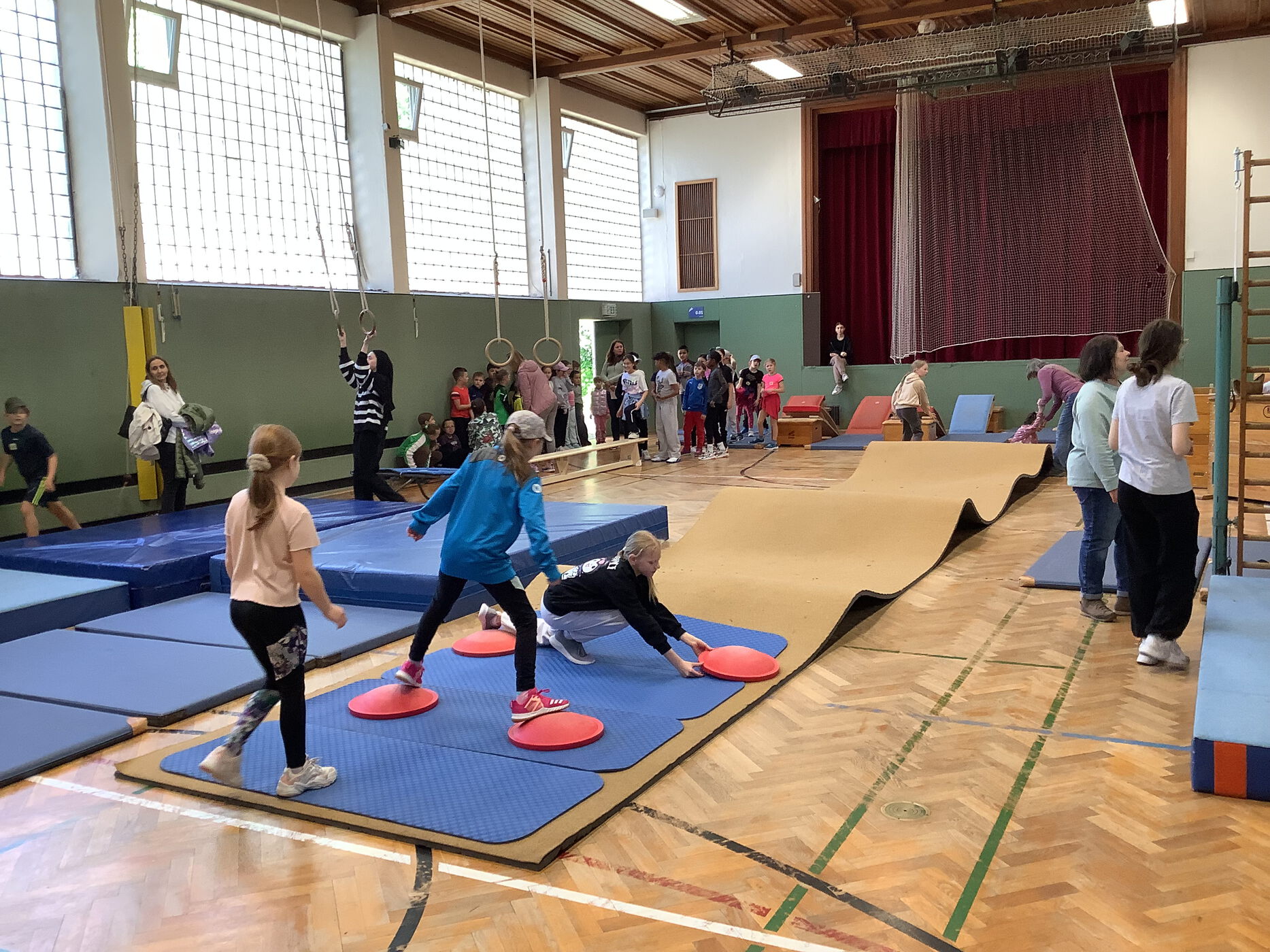 Kinder meistern einen Parcour. Sie klettern über Sprossenwände und Matten. Sie schwingen an Seilen und balancieren über Bänke.